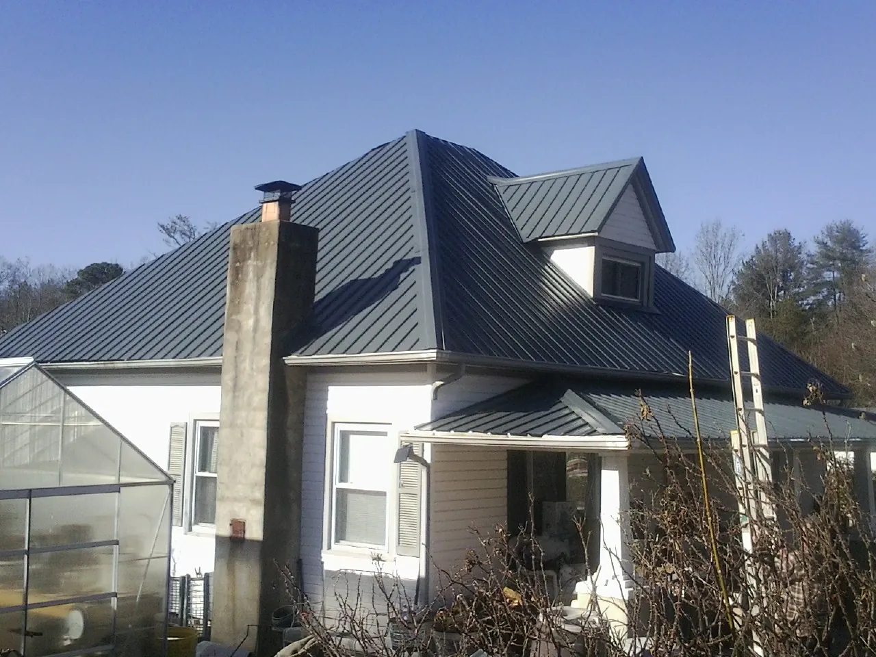 Dark blue standing seam metal roof on a white farmhouse with dormer — Slate & Tile Roof Repair by Roofing Brothers in Cedarbluff