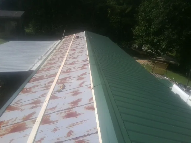 Old rusted panels beside newly installed green metal roofing — Wind Damage Roof Repair by Roofing Brothers in Cedarbluff
