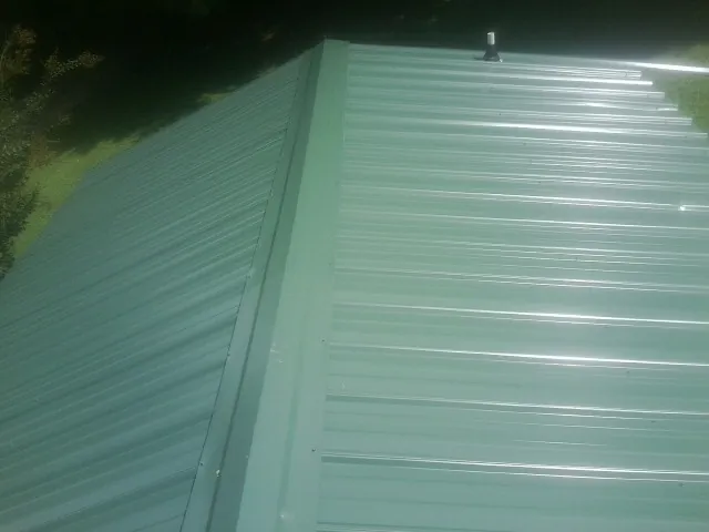 New green metal panels meeting at the ridge of a roof — Flat Roof Repair work by our crew in Cedarbluff