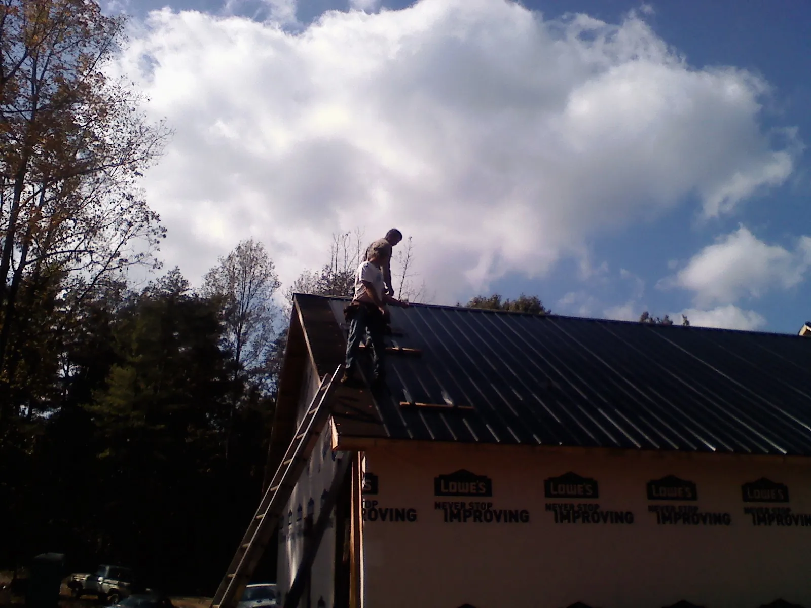 Roofer fastening dark metal panels high against a cloudy sky, from a Roof Inspection job in Cedarbluff